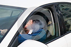 Young man in a blue jacket smokes an electronic cigarette while driving a car