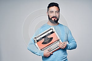 Young man in blue pullover standing holding retro typewriter