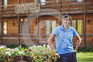 A young man in a blue shirt and blue shorts near decorative wooden carts with flowers, on a background of rustic style