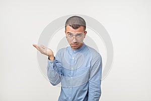Young man in blue shirt standing disorientated bewildered isolated on gray wall background. Decision making concept.