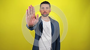 Young man in blue shirt and white T-shirt looks at camera, holds out his hand in front of him and says stop