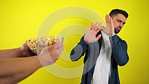 A young man in a blue shirt and white T-shirt is refuses the proposed a glass plate with popcorn, junk food