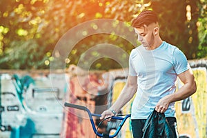 A young man with a BMX bike stands on the graffiti wall background. Portrait of BMX rider. Street culture. Sunshine