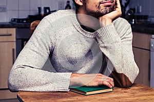 Young man with book daydreaming in kitchen