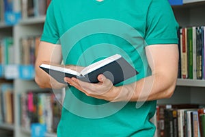 Young man with book near shelving unit in library