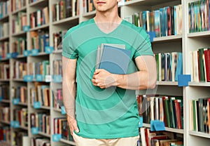 Young man with books near shelving unit in library