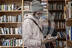 Young man in a bookstore. A brunette with glasses and a hat holds a book in her hands. Education, science and knowledge