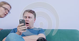 Young man with bored look uses smartphone, but suddenly sees shocking news. He opens his eyes and mouth wide in surprise
