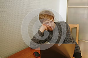 Young man bored while working at the computer