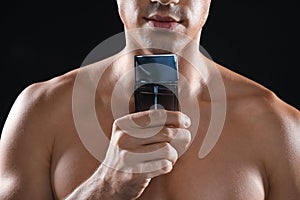 Young man with bottle of perfume on black background