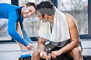 Young man with bottle of water sitting on tyre and talking to friend