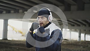 Young man boxer in headphones training punches in urban location outdoors in winter