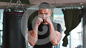 Young man boxer passing by the punching bag and stands in the protective stance