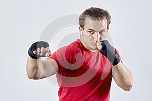 Young man boxes, making hook with right hand. Black bandages, red T-shirt, determined face expression, strong emotions.