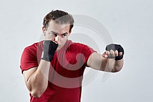 Young man boxes, making jab with left hand. Black bandages, red T-shirt, determined face expression, strong emotions.