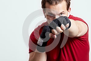 Young man boxes, making jab with left hand. Black bandages, red T-shirt, determined face expression, strong emotions.