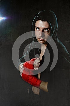 Young man in boxing hoodie jumper with hood on head wearing hand and wrist wrapped ready for fighting posing isolated