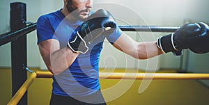 Young man boxing workout on ring in a fitness club. Caucasian male boxer in black gloves. Muscular strong man on