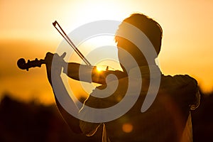 Young man or boy playing the violin at sunset