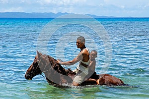 Young man with a boy riding horse on the beach on Taveuni Island
