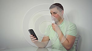 A young man breathes through an inhaler mask with a phone in his hands. A man wearing glasses and an oxygen mask is