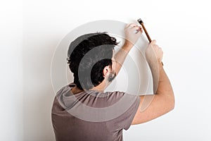 Young man bricolage hammering nail wall