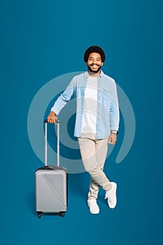 A young man with a bright smile leans casually on his modern suitcase