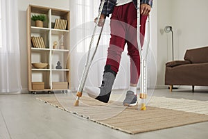 Young man with broken foot wearing leg support brace and walking on crutches at home