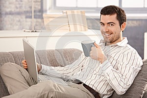Young man browsing Internet at home smiling