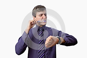 Young man brushing his teeth also looks on at watch on white background