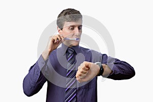 Young man brushing his teeth also looks on at watch on white background