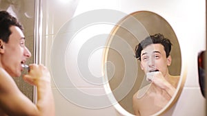 Young man brushing his teeth in bathroom. health care, dental hygiene, people and beauty concept - smiling young man