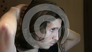 Young man brushing long layered dark brown hair in bathroom standing in front of mirror, side view,