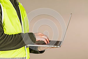 A young man, a Builder in the green safety vest, using a computer, on a gray background. Technology in industrial works