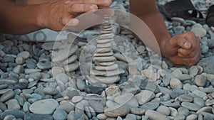 A young man builds a pebble tower on the beach, and then it falls. Tower close-up.