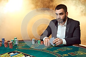 A young man in a business suit sitting at the poker table. Man gambles. The player at the gaming table playing cards.