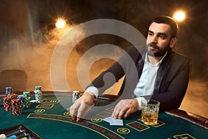 A young man in a business suit sitting at the poker table. Man gambles. The player at the gaming table playing cards.