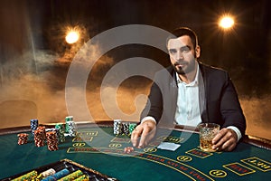 A young man in a business suit sitting at the poker table. Man gambles. The player at the gaming table playing cards.