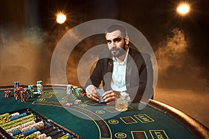 A young man in a business suit sitting at the poker table. Man gambles. The player at the gaming table playing cards.