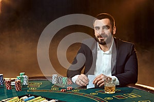 A young man in a business suit sitting at the poker table. Man gambles. The player at the gaming table playing cards.