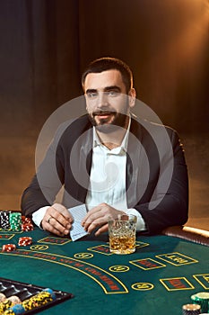 A young man in a business suit sitting at the poker table. Man gambles. The player at the gaming table playing cards.