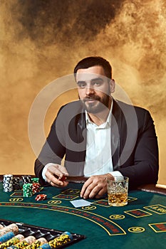 A young man in a business suit sitting at the poker table. Man gambles. The player at the gaming table playing cards.