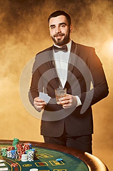 A young man in a business suit standing near poker table. Man gambles.