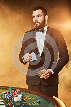 A young man in a business suit standing near poker table. Man gambles.