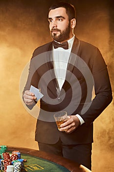 A young man in a business suit standing near poker table. Man gambles.