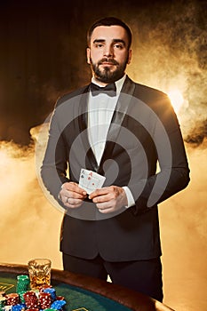 A young man in a business suit standing near poker table. Man gambles.