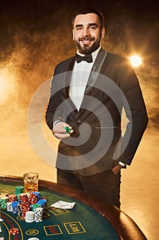A young man in a business suit standing near poker table. Man gambles.