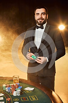 A young man in a business suit standing near poker table. Man gambles.