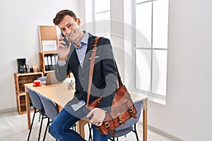 Young man business worker talking on smartphone sitting on table at office