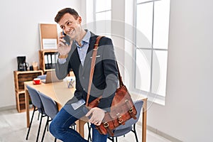 Young man business worker talking on smartphone sitting on table at office